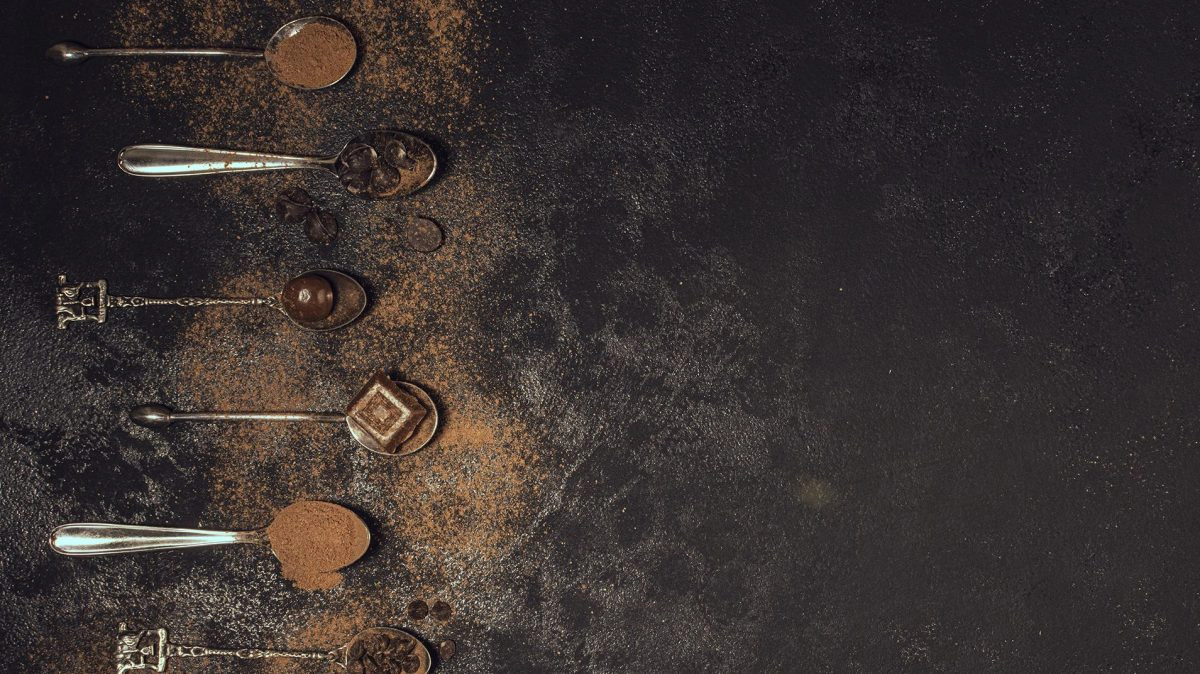 Šest kašika na kojima se nalaze različiti proizvodi od kakaoa na crnoj pozadini.