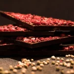 Tamna Aguara čokolada poređana jedna na drugu sa posutim voćem i zrnima bivera oko njih.