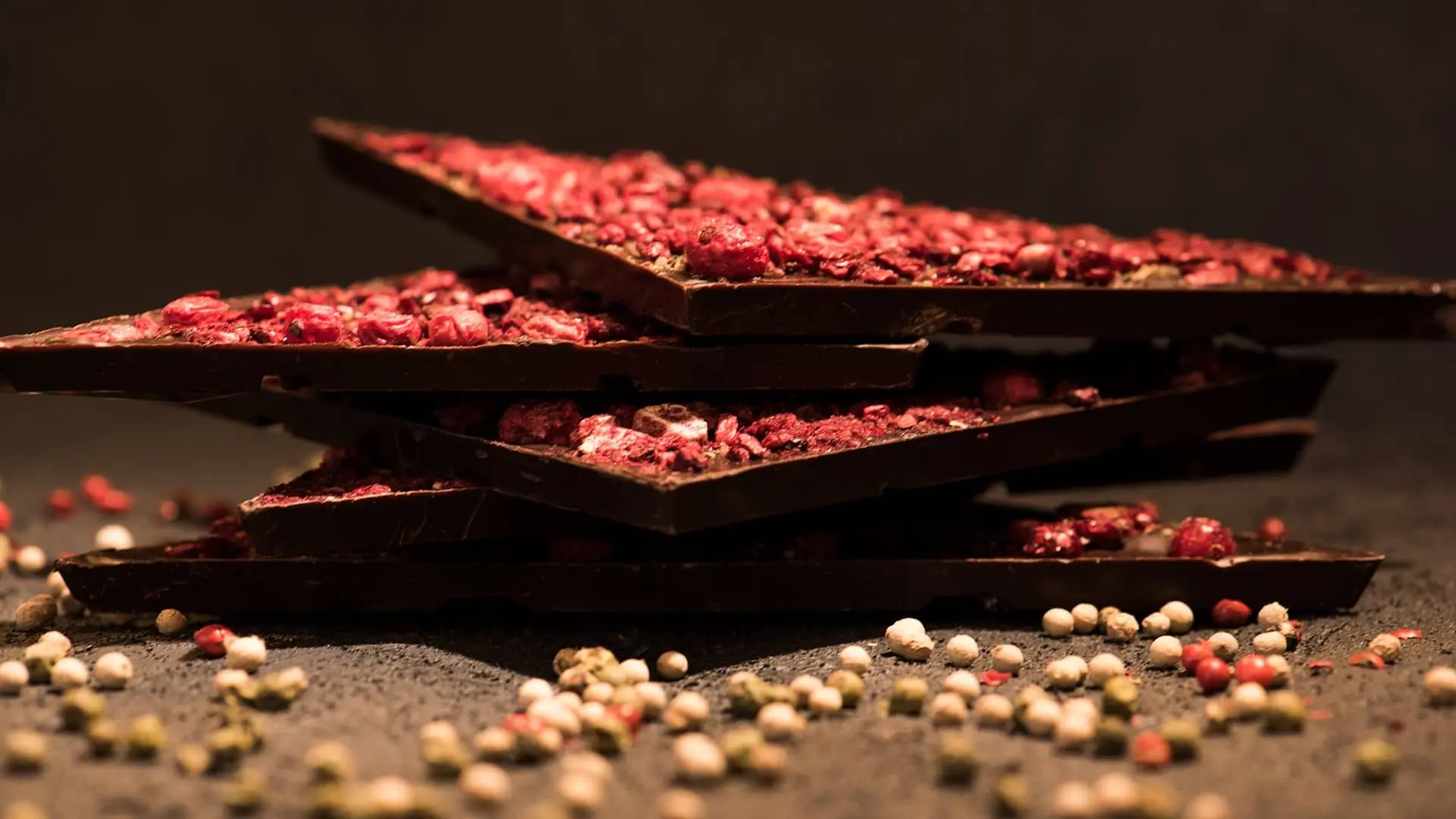 Tamna Aguara čokolada poređana jedna na drugu sa posutim voćem i zrnima bivera oko njih.