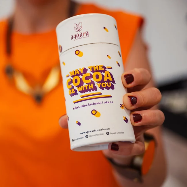 Aguara kakao prah May the cocoa be with you koga drži ženska osoba u bluzi narandžaste boje.