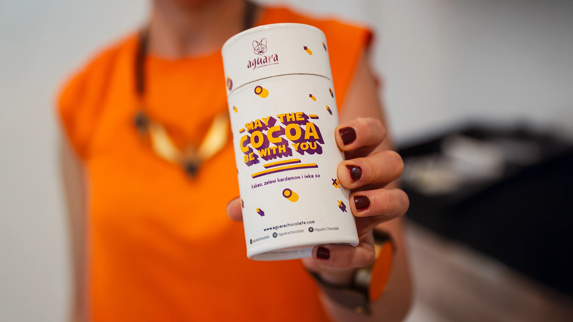 Aguara kakao prah May the cocoa be with you koga drži ženska osoba u bluzi narandžaste boje.